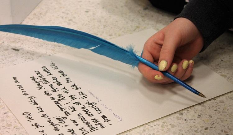 En hand med en blå fjäderpennas skriver dagbok.